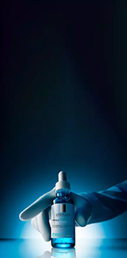 Hyalu B5 Serum bottle held in hand on blue background
